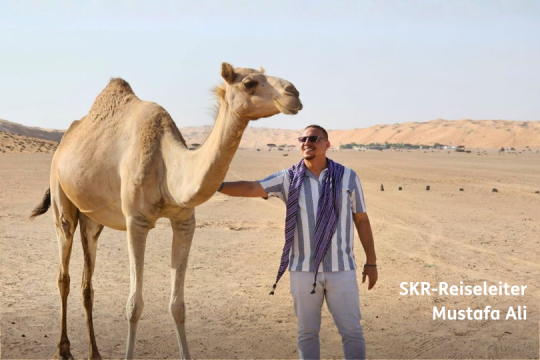 Mann steht neben Kamel, Reiseleiter für SKR